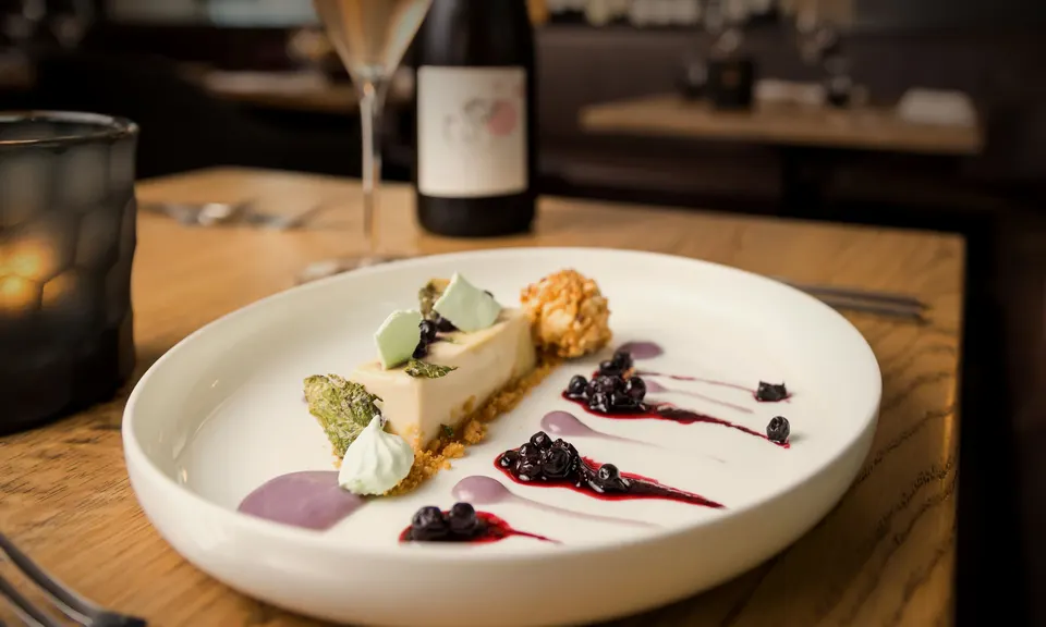 Dessert am gedeckten Tisch, dahinter eine Flasche Wein