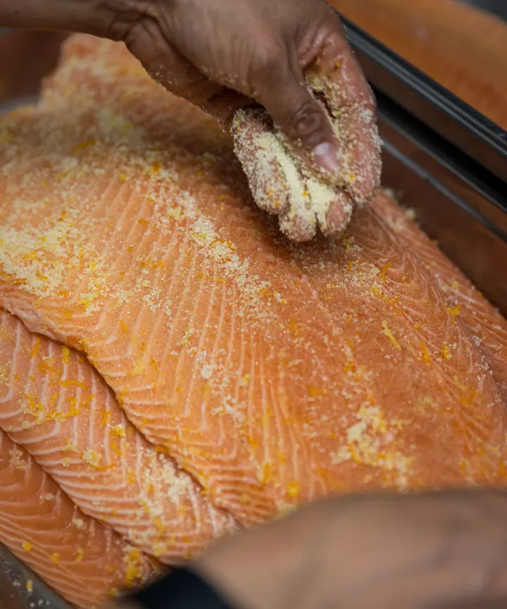Eine Hand streut Beize über einen Lachs