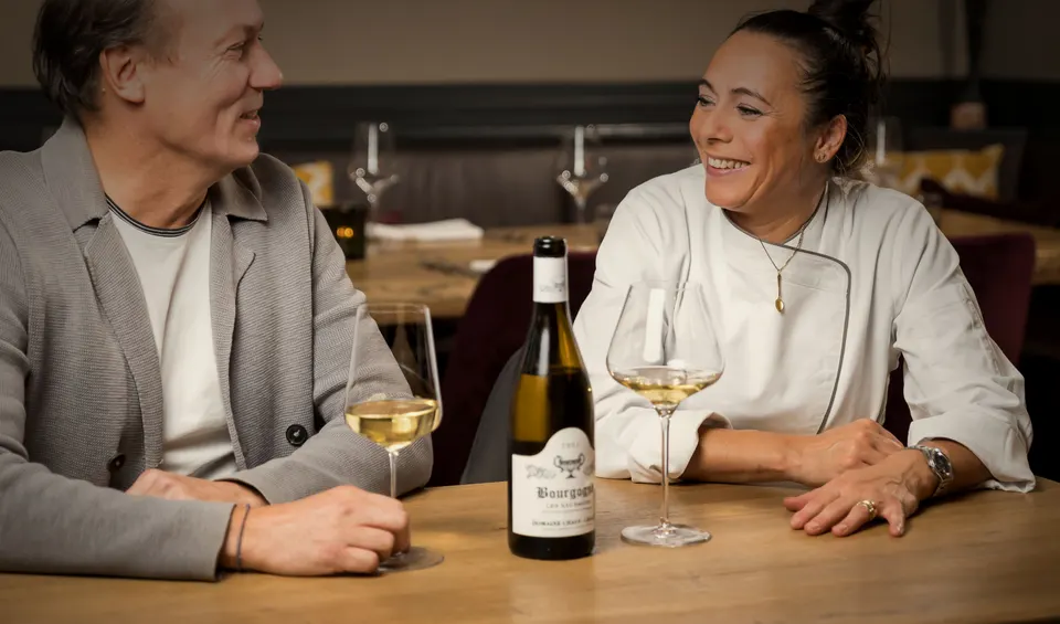 Patrick Fischbacher und Claudia De Luca im Gespräch am Tisch, ein Glas Weißwein vor sich