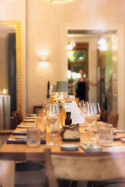 Die gedeckte lange Tafel mit Weingläsern, Brot und Menükarte, im Hintergrund die offene Tür