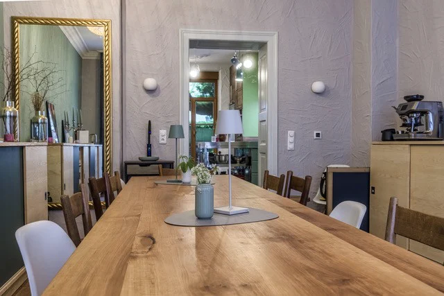 Die lange Holztafel mit Vase und Tischleuchte, dahinter ein Goldspiegel und die Tür zur Küche