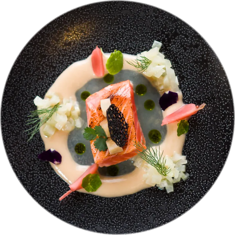 Lachs mit Kaviar-Chip auf dunklem Teller, von oben
